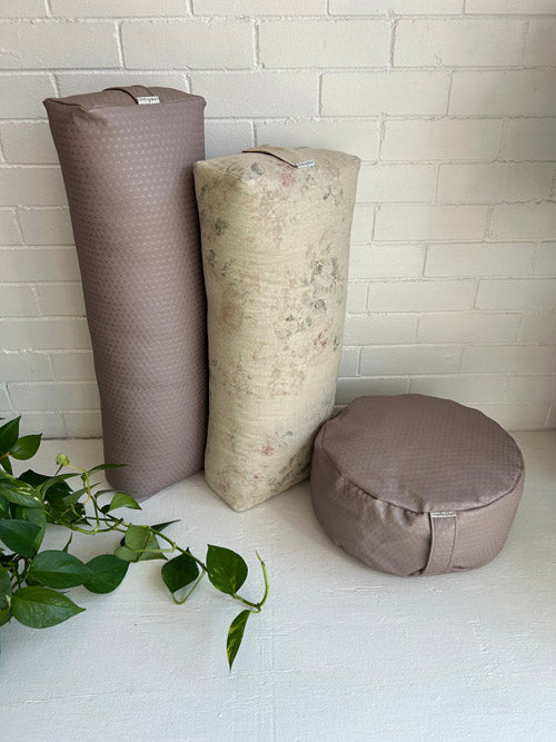 Yoga bolsters and a meditation cushion against a white brick wall.