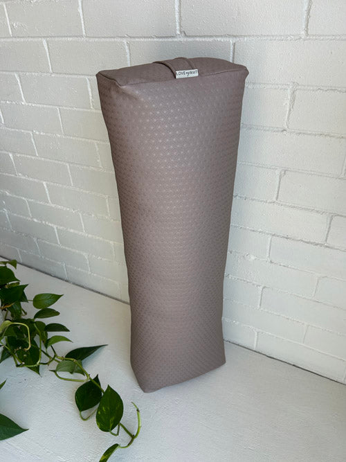 Mauve textured vinyl yoga bolster on a white surface with a white brick wall background