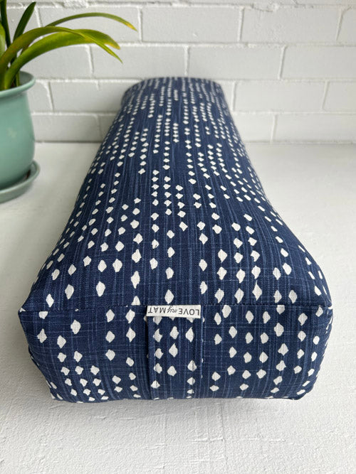 Blue and white patterned yoga bolster on a white surface with a plant in the background