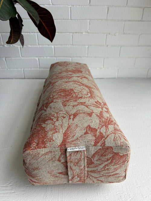 Fabric-covered Long Yoga Bolster with floral pattern against a white brick wall