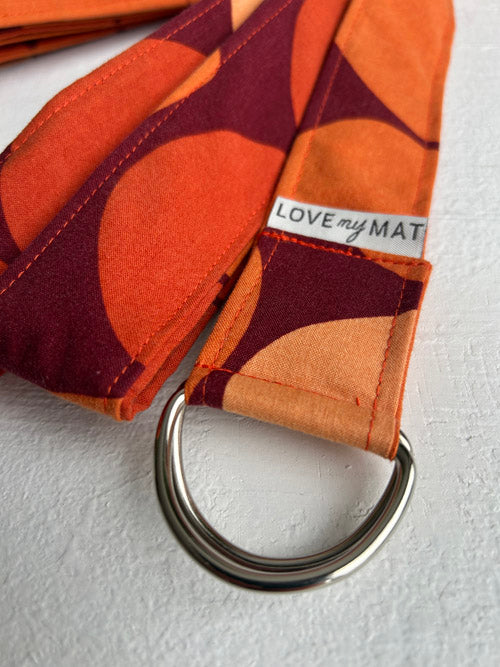 Orange and dark red patterned yoga strap with a metal ring on a white background