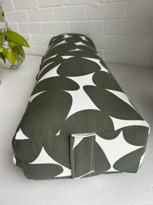 Green and white patterned bolster on a light surface with a plant in the background