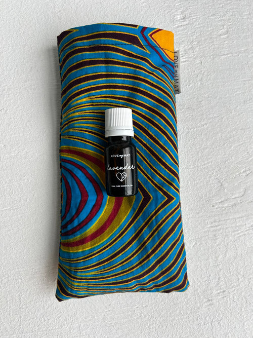 Colourful fabric eye pillow with a small brown bottle labeled 'lavender' on a textured white background