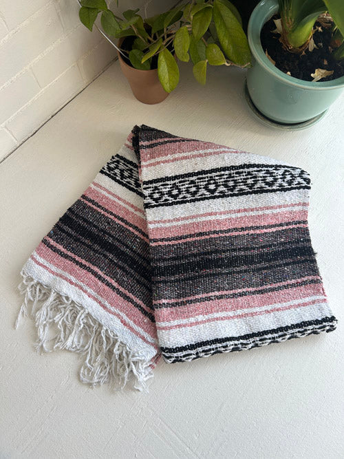 Striped towel with fringes on a white surface with potted plants in the background