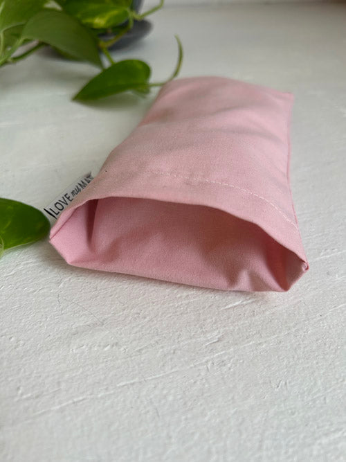 Pink fabric eye pillow on a light gray surface with green leaves in the background