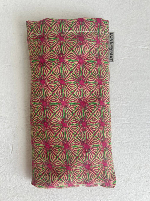 Pink and Green Abstract Sun-like fabric eye pillow on a white surface.