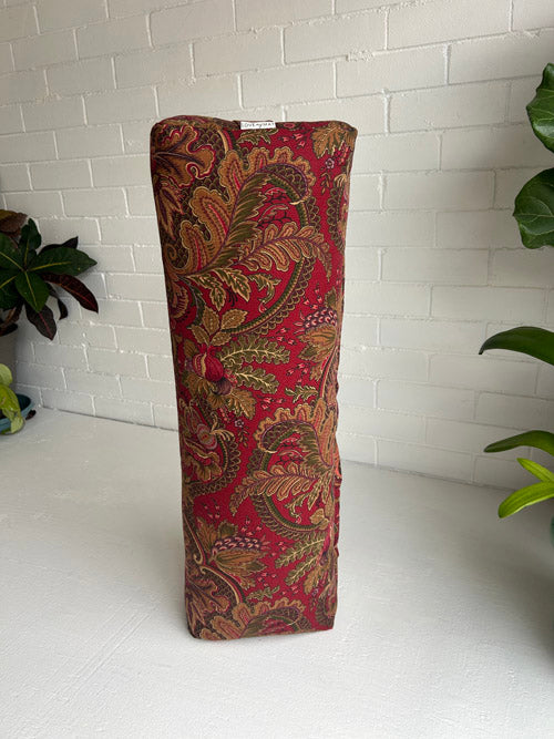 Red and gold patternedY oga  Bolster on a white surface with a white brick wall background