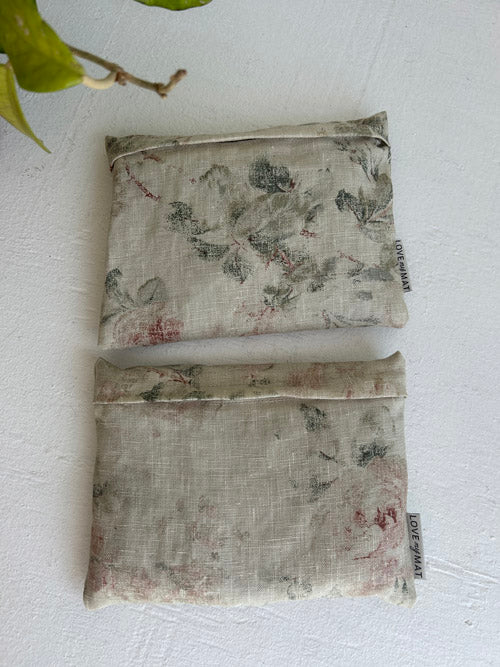 Two floral-patterned fabric hadnweights on a textured white surface with a leaf in the corner.