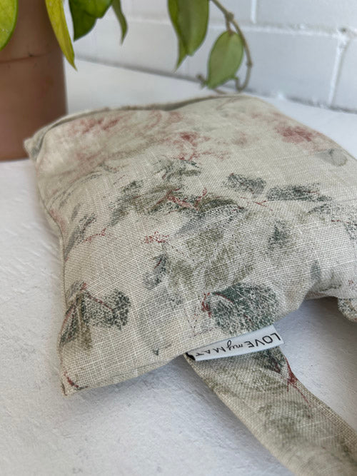 Floral-patterned fabric sandbag on a white surface with a plant in the background