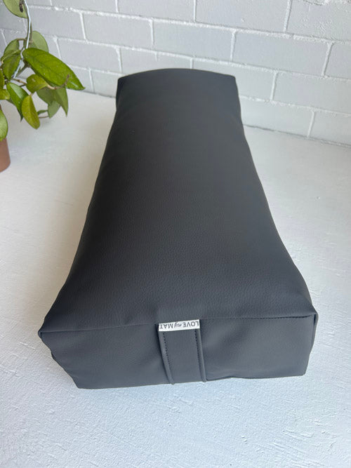 Gray yoga cushion on a white surface with a plant in the corner