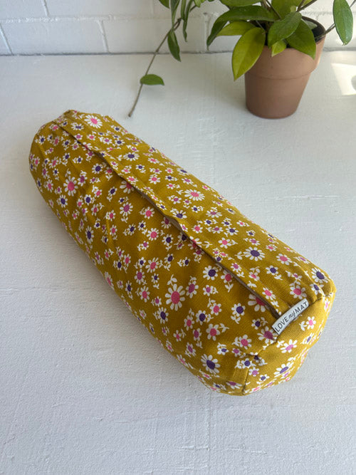 Floral-patterned small round yoga bolster on a white surface with a plant in the background
