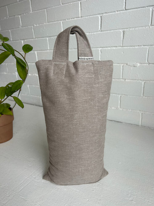 Taupe coloured Sandbag Standing on a white surface and background with a plant near by
