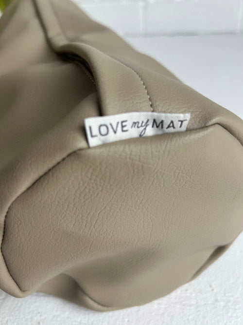Close up of a sand coloured round small yoga bolster on a white surface and against a white brick wall