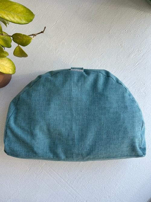 Teal Yoga or Meditation Cushion on a white surface with a plant in the corner