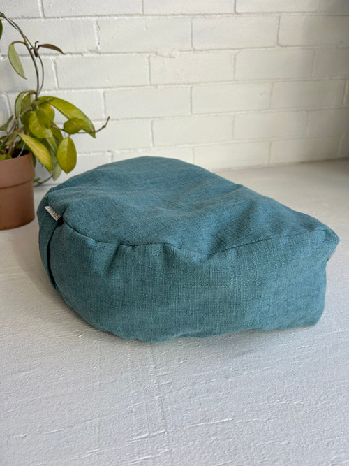 Teal Meditation Cushion on a white surface with a white brick wall in the background
