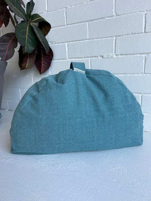 Teal meditation pillow on a white surface with a white brick wall background