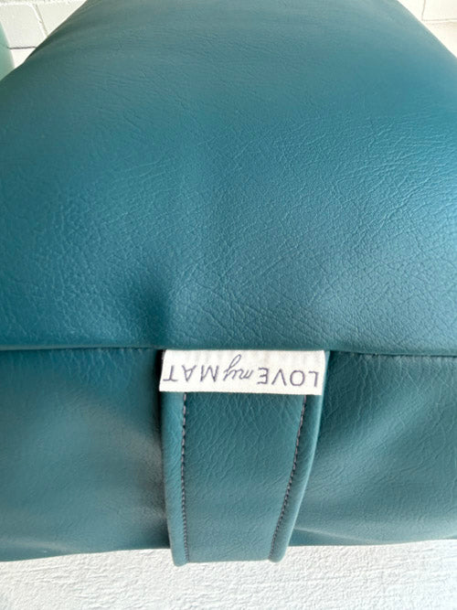 Teal leather yoga bolster with a label reading 'LOVE my MATE' on a white background