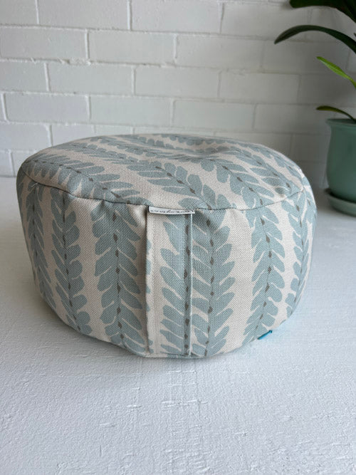 Round ottoman with leaf pattern on a white surface and light gray tiled wall background