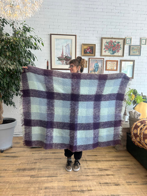 Person holding a plaid blanket in a room with framed pictures on the wall.
