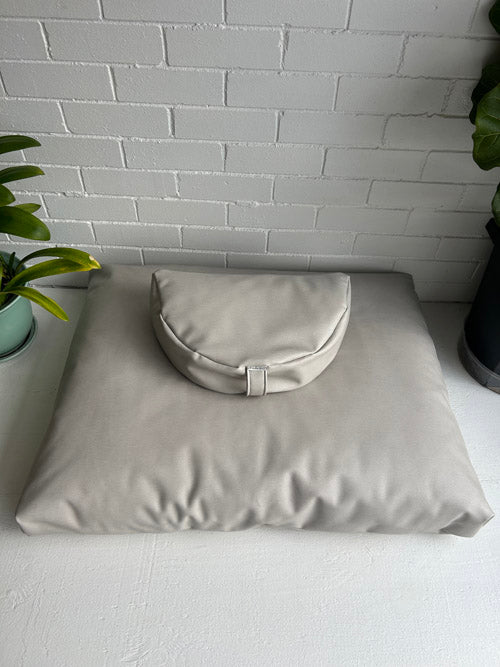 Vinyl beige meditation cushions placed against a white brick wall.