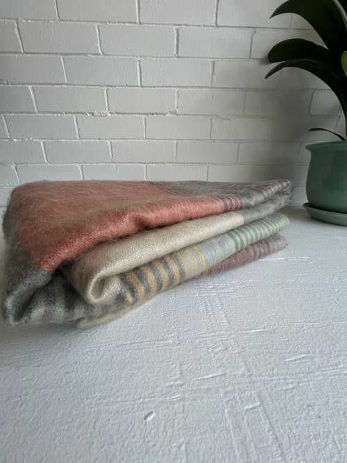 Folded blanket in various colors on a white surface with a plant in the corner.