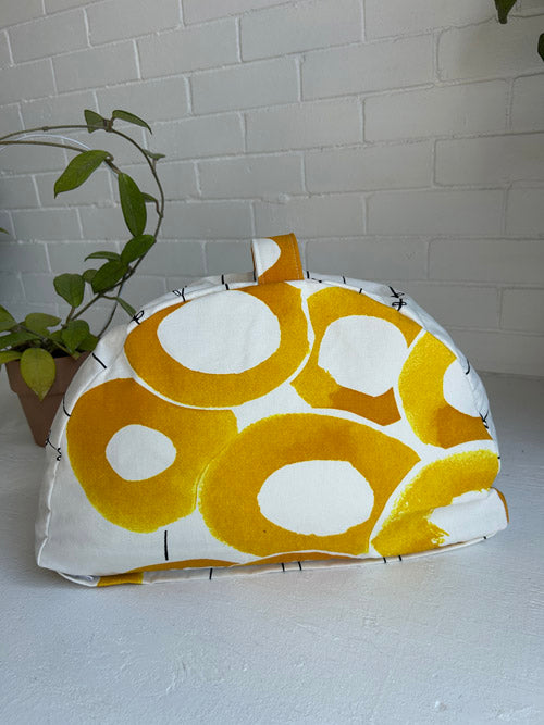Yellow and white patterned fabric sit cushion on a light surface with a plant in the background