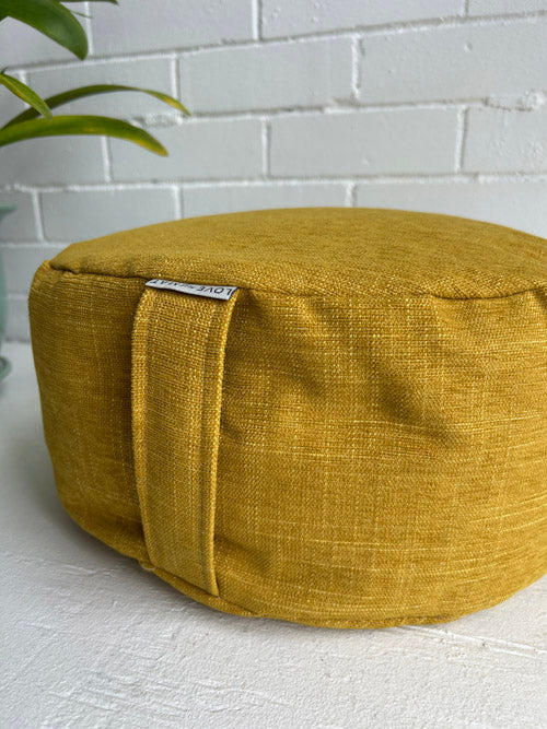 Yellow fabric meditation cushion on a white surface with a white brick wall background