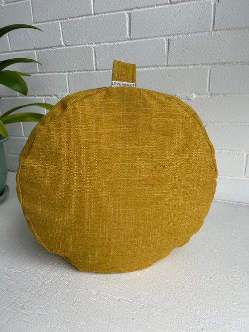 Round mustard yellow meditation cushion on a white surface with a white brick wall background