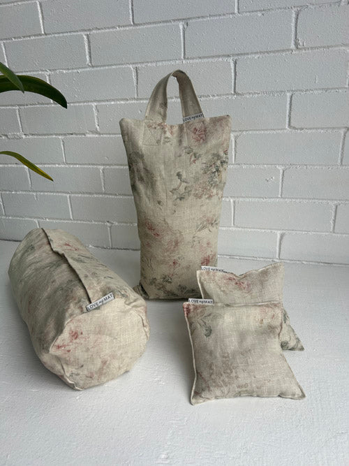 Yogie Prop Bundle of 10lb fabric sandbag, mini round bolster, and knee pillows on a white surface against a white brick wall.