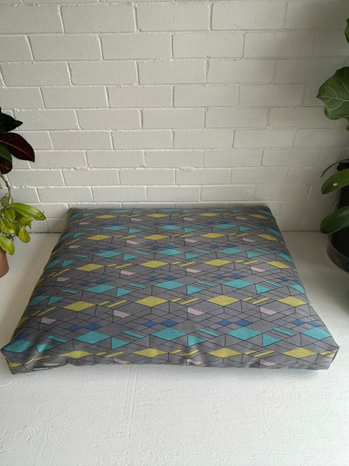 Patterned floor cushion on a white surface with a light gray tiled wall background