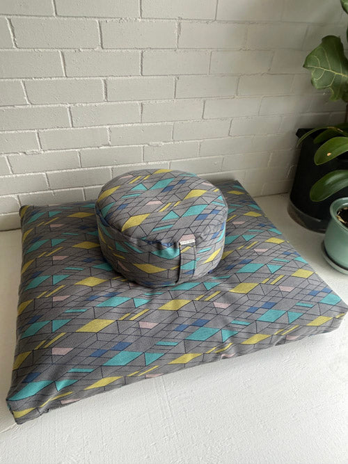 Gray geometric-patterned cushion with a matching round pillow on a white surface.