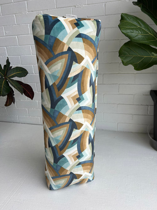 Decorative bolster with geometric pattern on a white surface with plants in the background