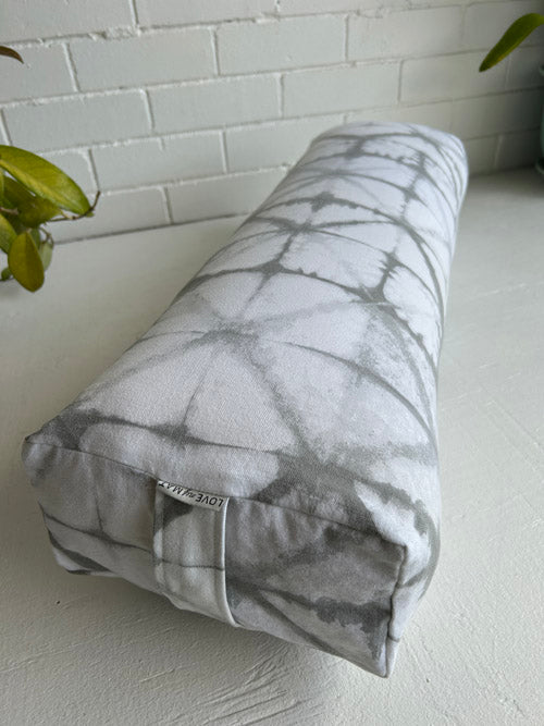 Gray and white marble-patterned yoga bolster against a white brick wall.